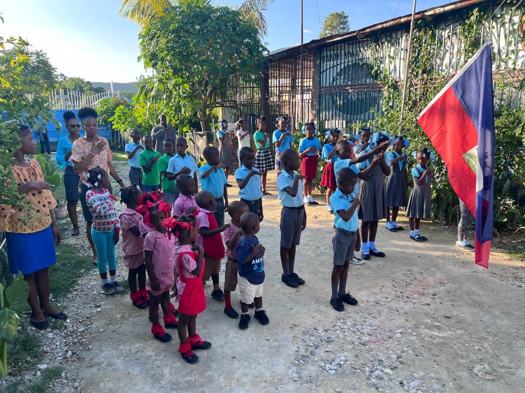 Students singing the national anthem beside the Haitian flag